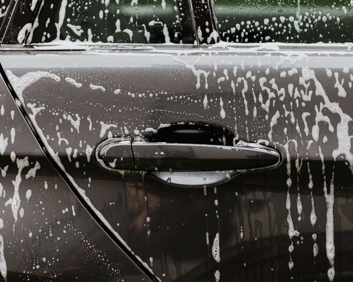 Mousse de lavage sur la portière d'une voiture sombre